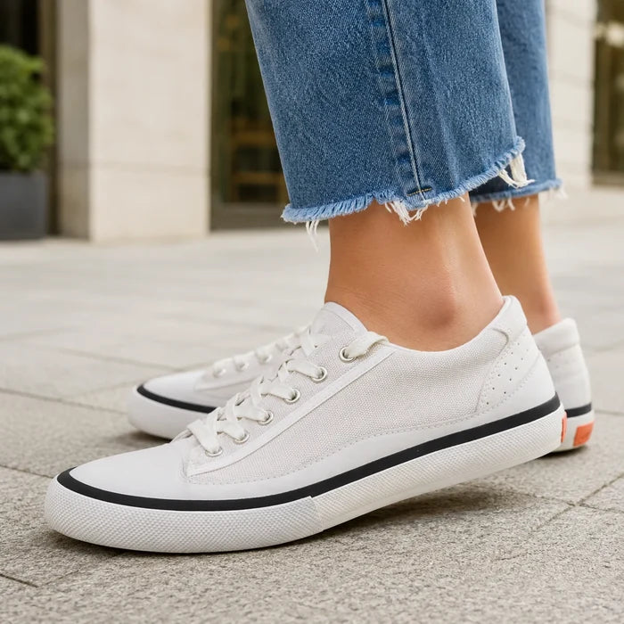 White lace-up low-top sneakers with black trim, worn with cuffed denim