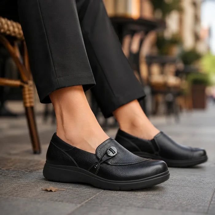 Black leather slip-on shoes with buckle strap, worn with cropped dark pants