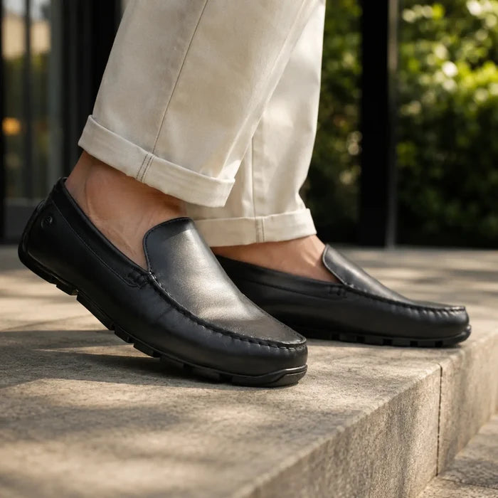 Black leather slip-on loafer on a man's foot with textured tread sole