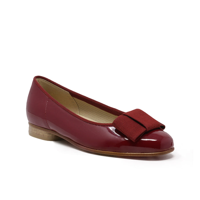 Red leather ballet flat with bow strap and low heel, glossy finish.