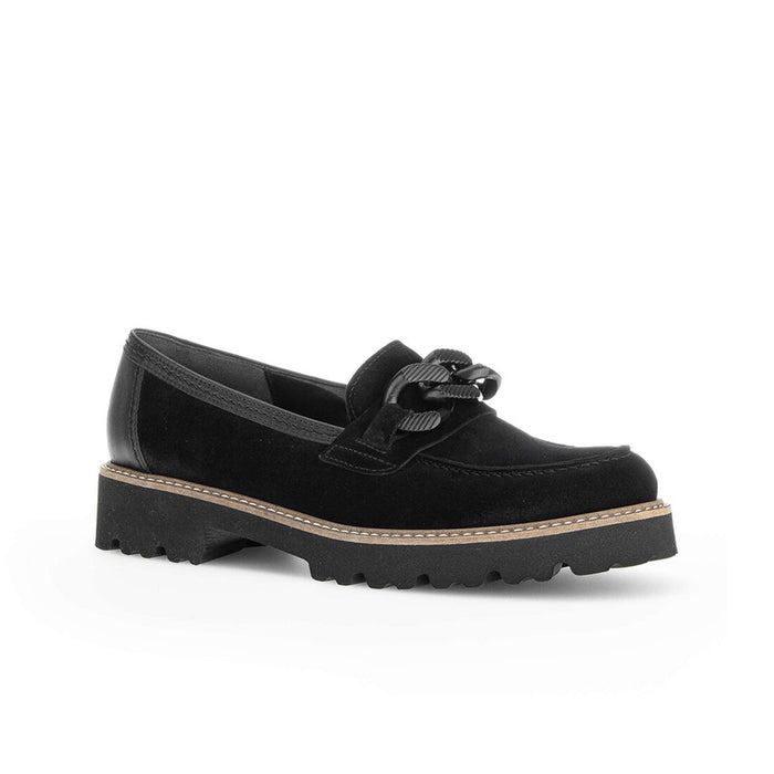 Black loafer with tassel-knot detail and chunky tread sole, tan welt stitching.